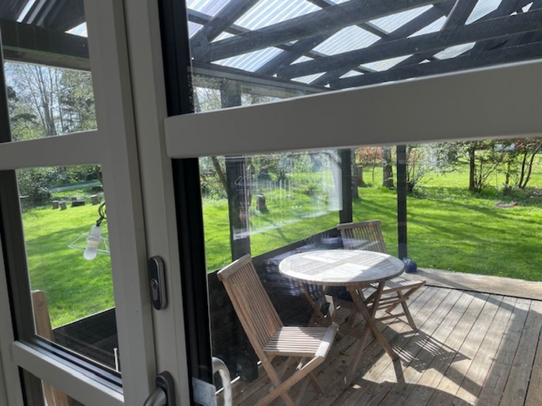 Kig fra stue til stor overdkket terrasse og have